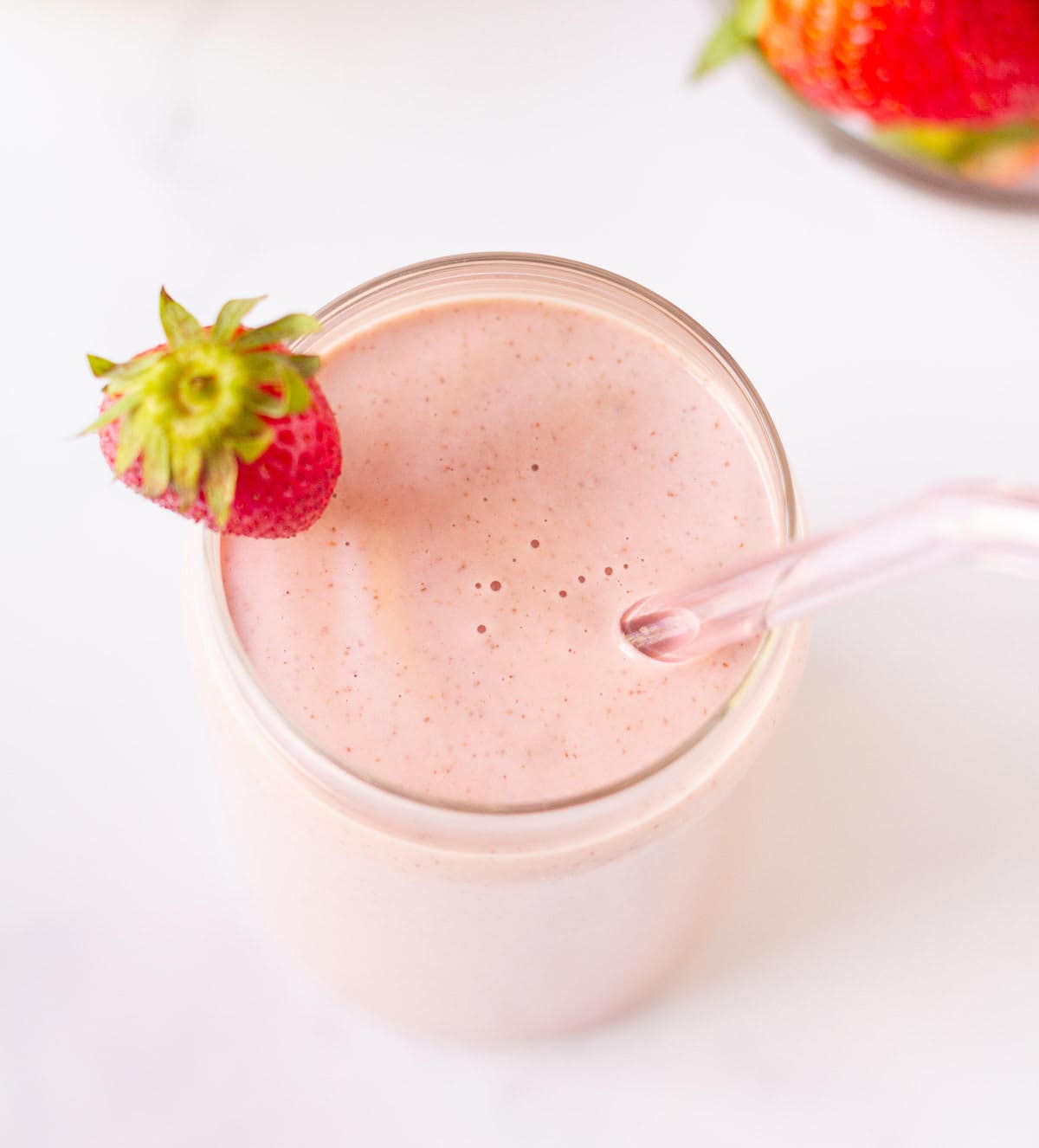 strawberry smoothie with a strawberry on the rim and a glass straw.