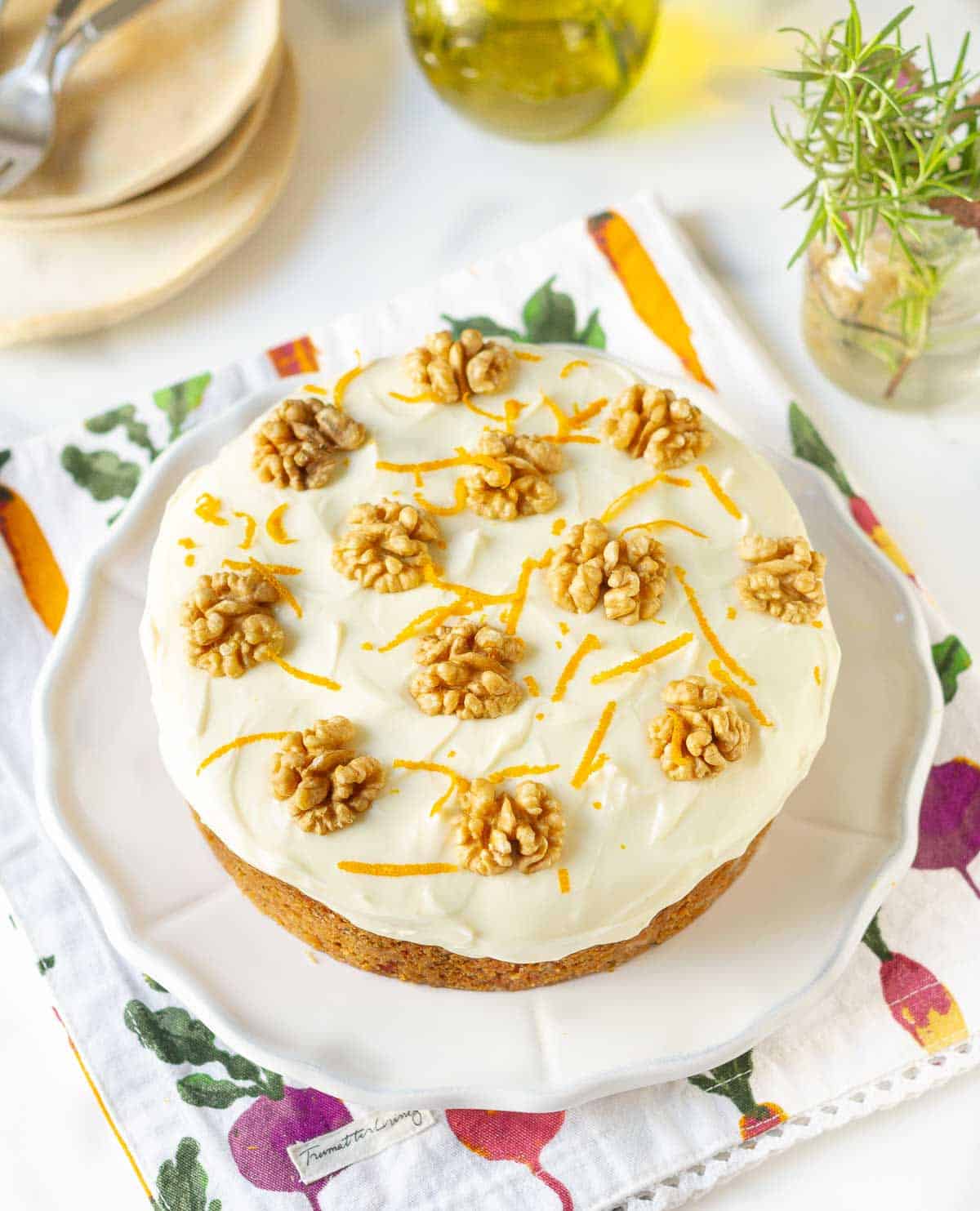 Carrot cake with frosting, walnuts and orange zest on a white platter.