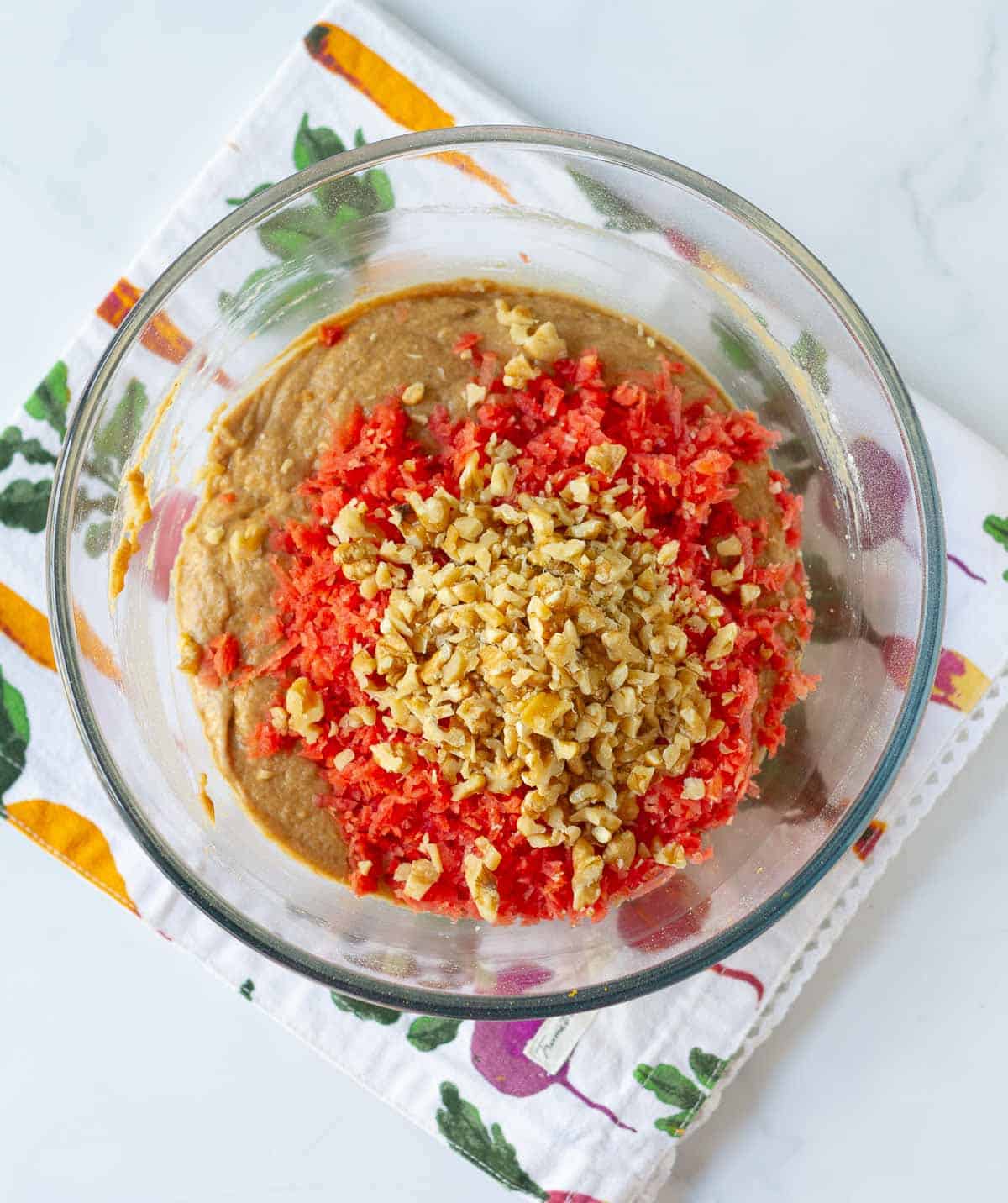 Shredded carrots and chopped walnuts on top of cake batter in a bowl.