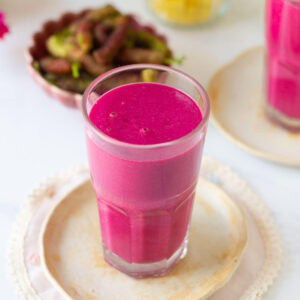 Mulberry mango smoothie in a glass on a small plate.