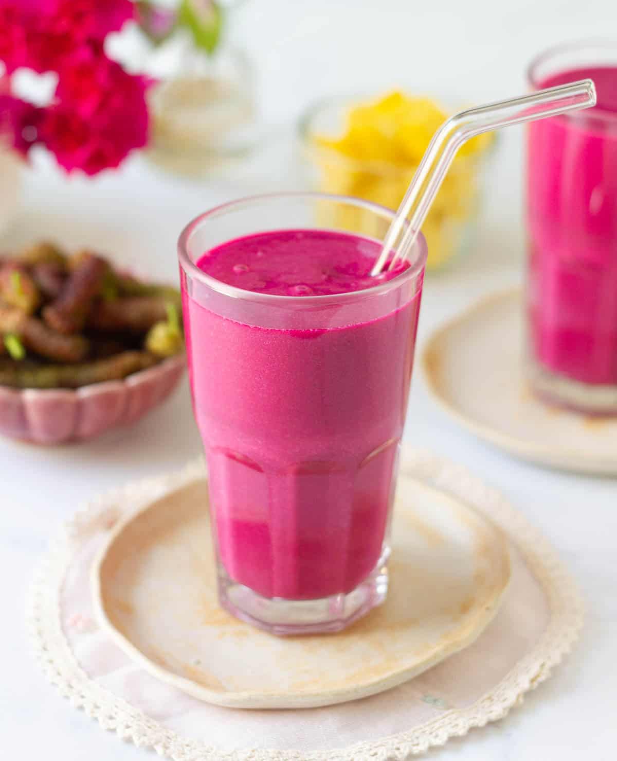 Mulberry mango smoothie in a glass with a glass straw.