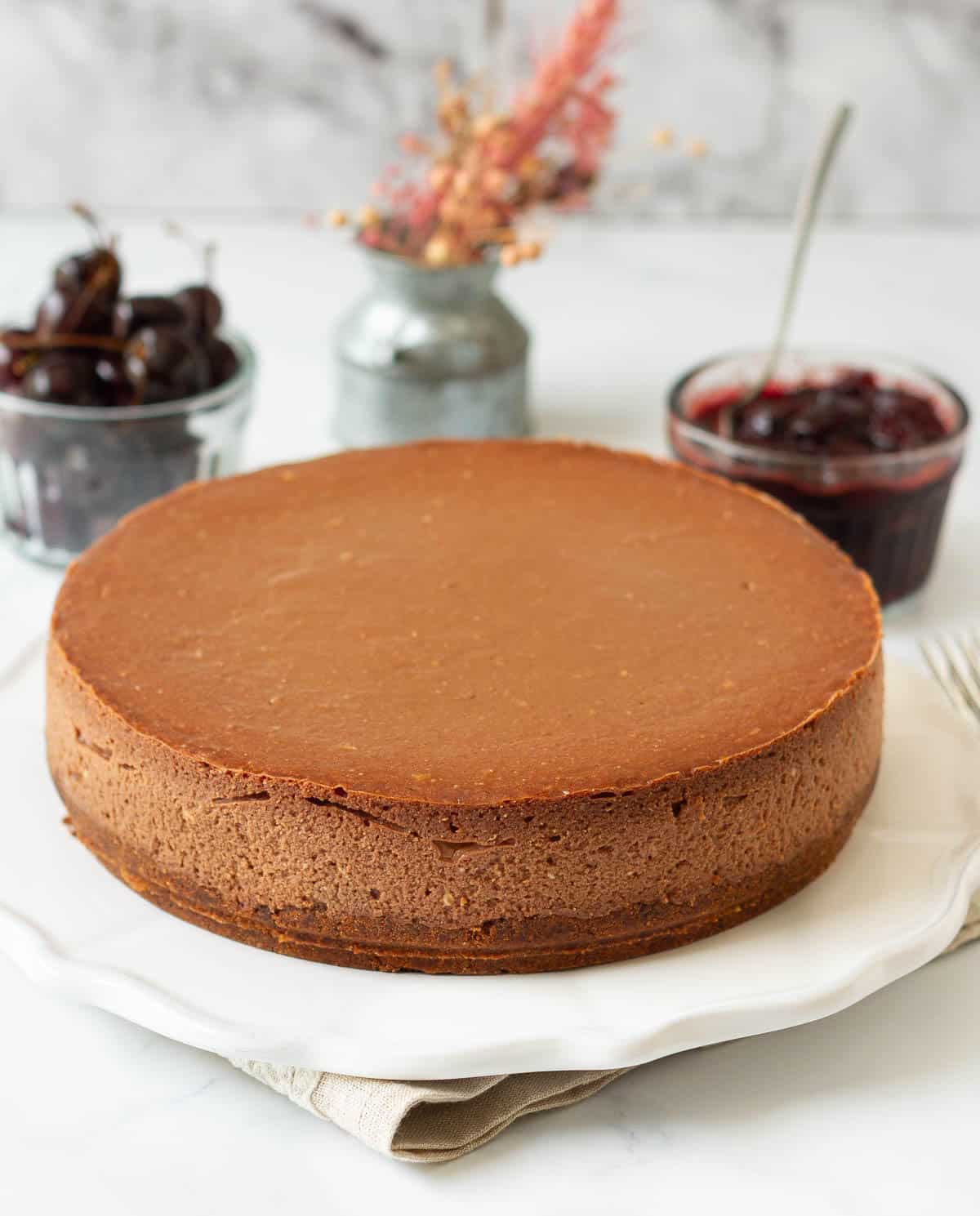 Chocolate cheesecake on a platter with ingredients in the background.