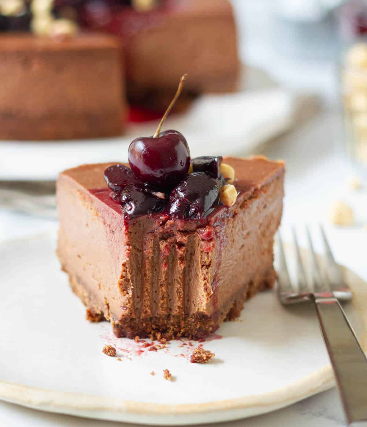 A bite taken from a slice of chocolate cheesecake on a plate with a fork.