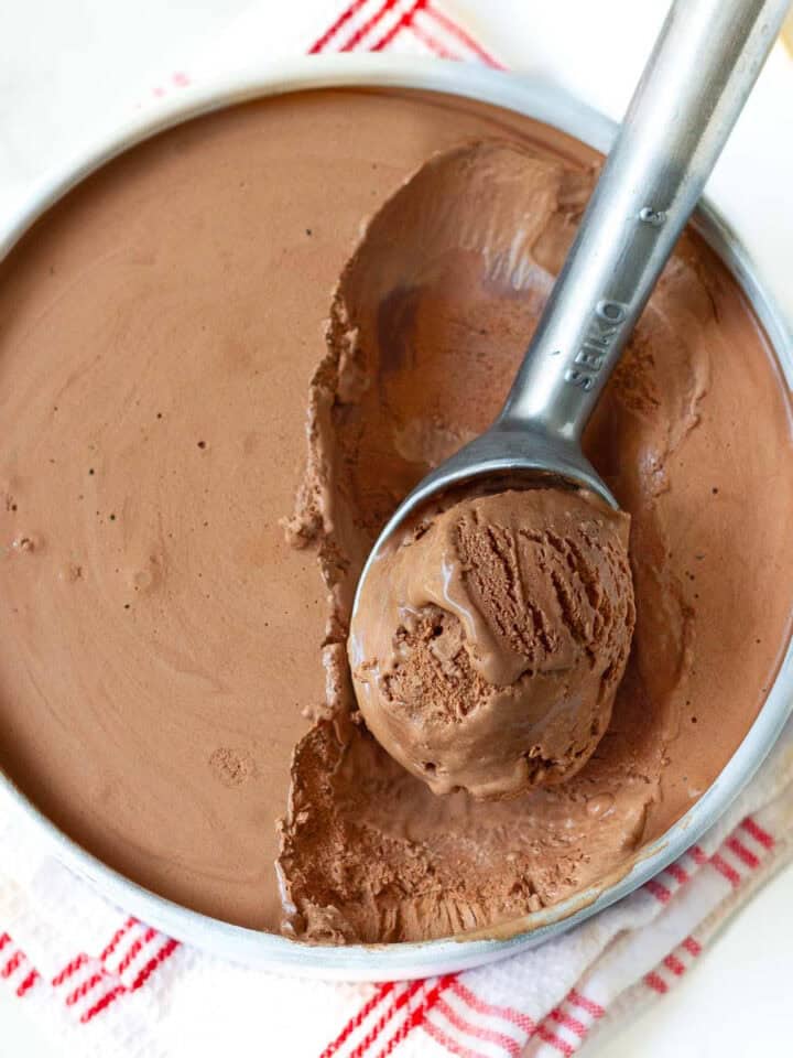 Ice cream in a pan with a scoop taken out with an ice cream scooper.