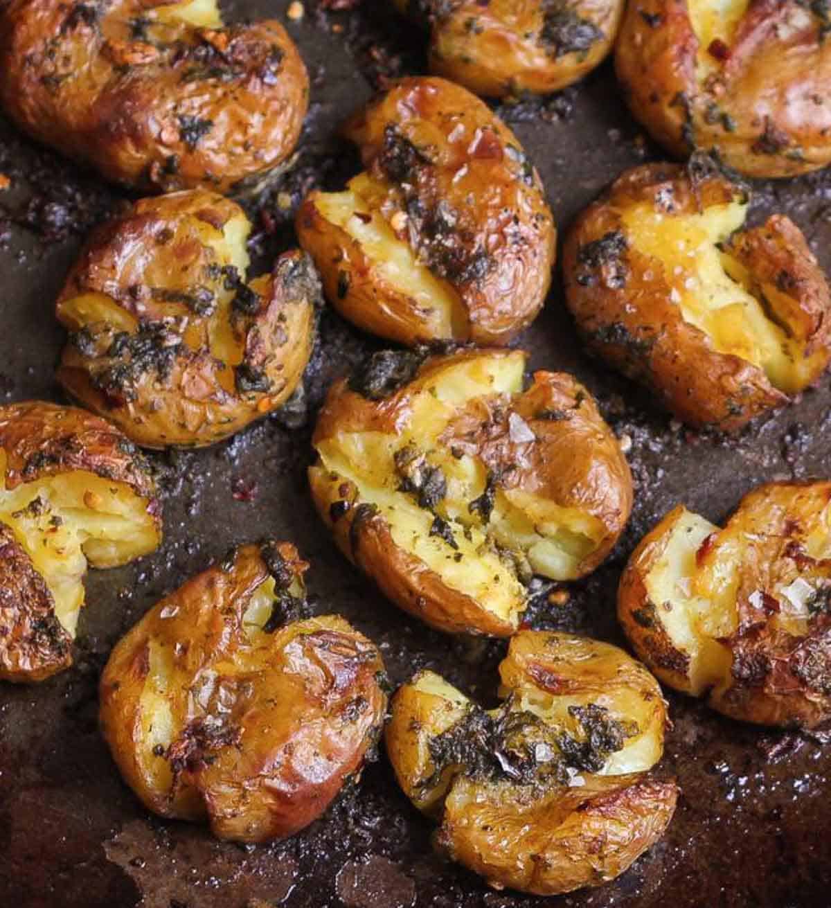 Crispy roasted potatoes with garlic and basil on a black baking tray.