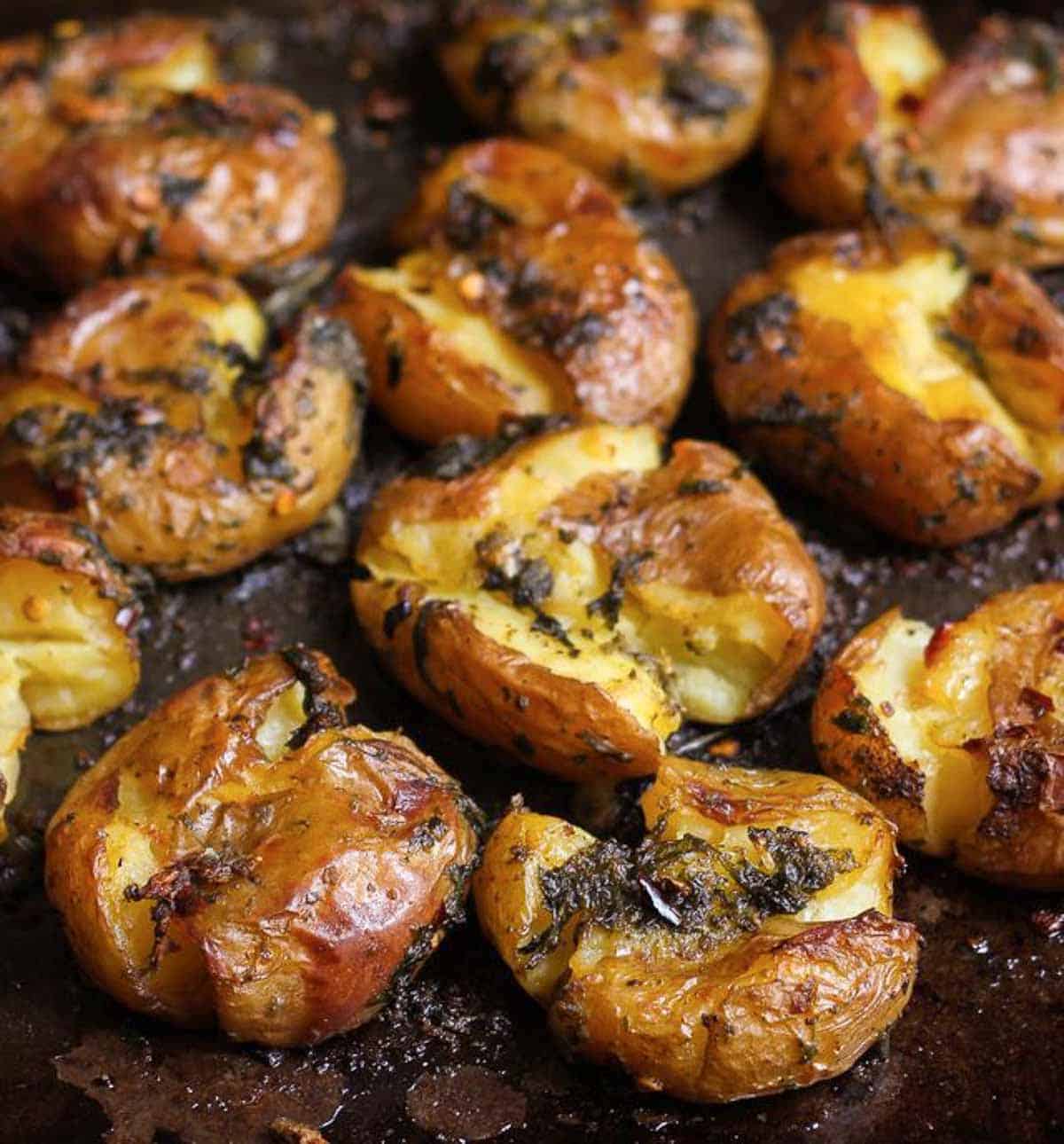 Baked smashed potatoes with basil-garlic mixture on a tray.