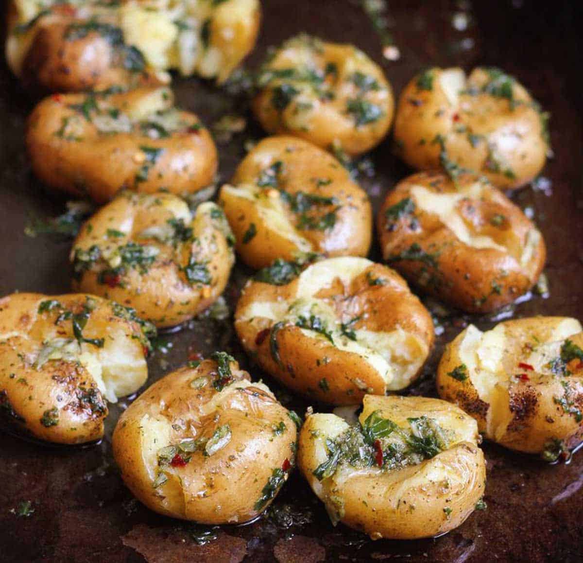 Smashed potatoes coated with basil garlic mixture on a baking tray.