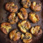 Crispy smashed potatoes with garlic and basil on a black tray.