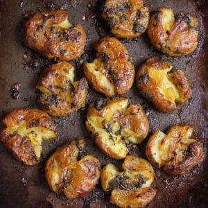 Crispy smashed potatoes with garlic and basil on a black tray.