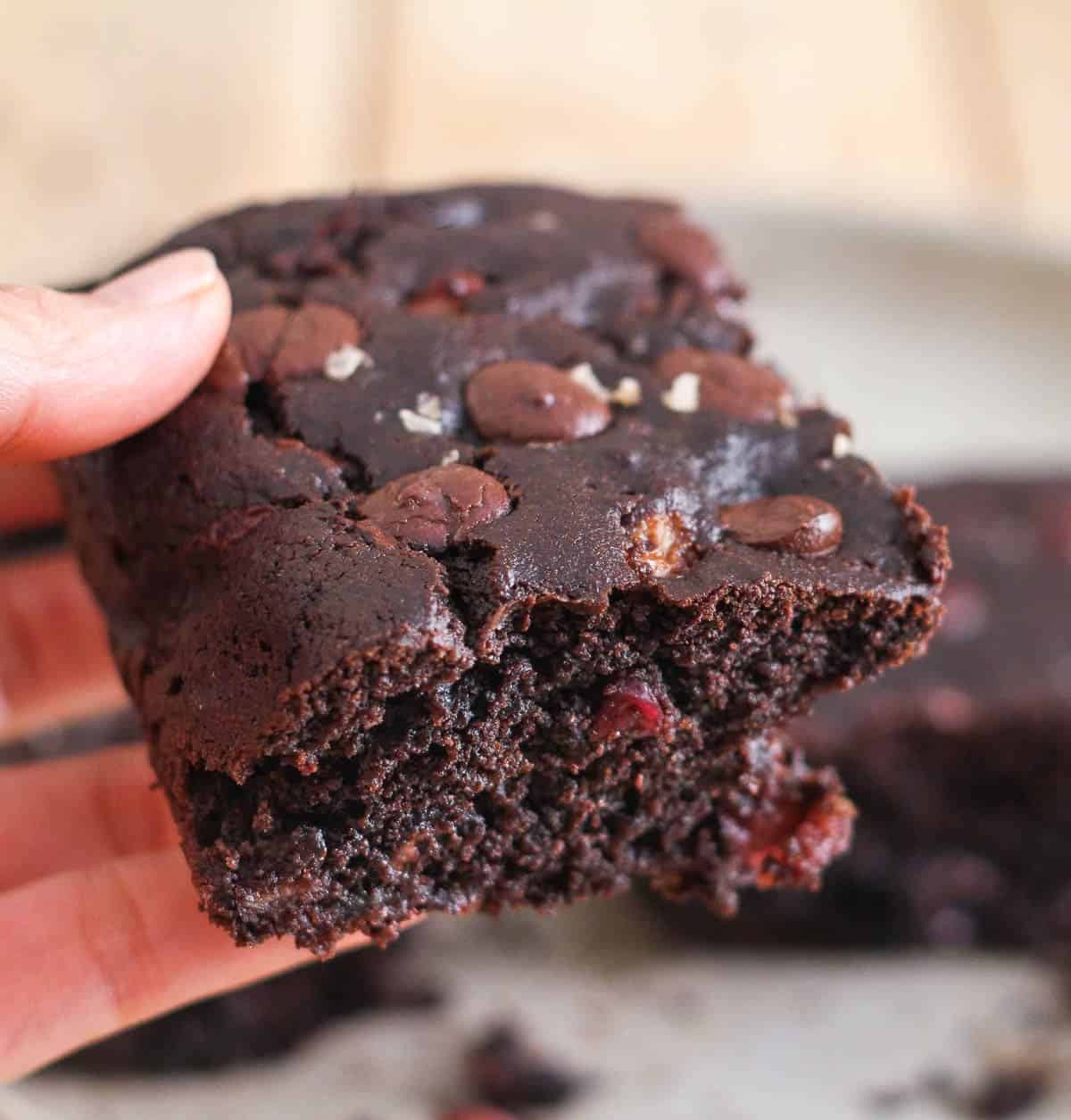 A hand holding a piece of chocolate cherry cake.
