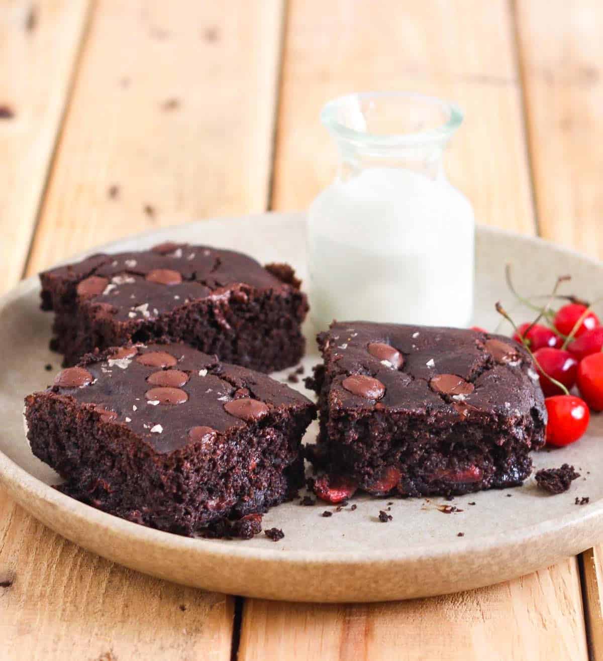 3 pieces of chocolate cherry cake on a platter with a milk bottle and cherries.