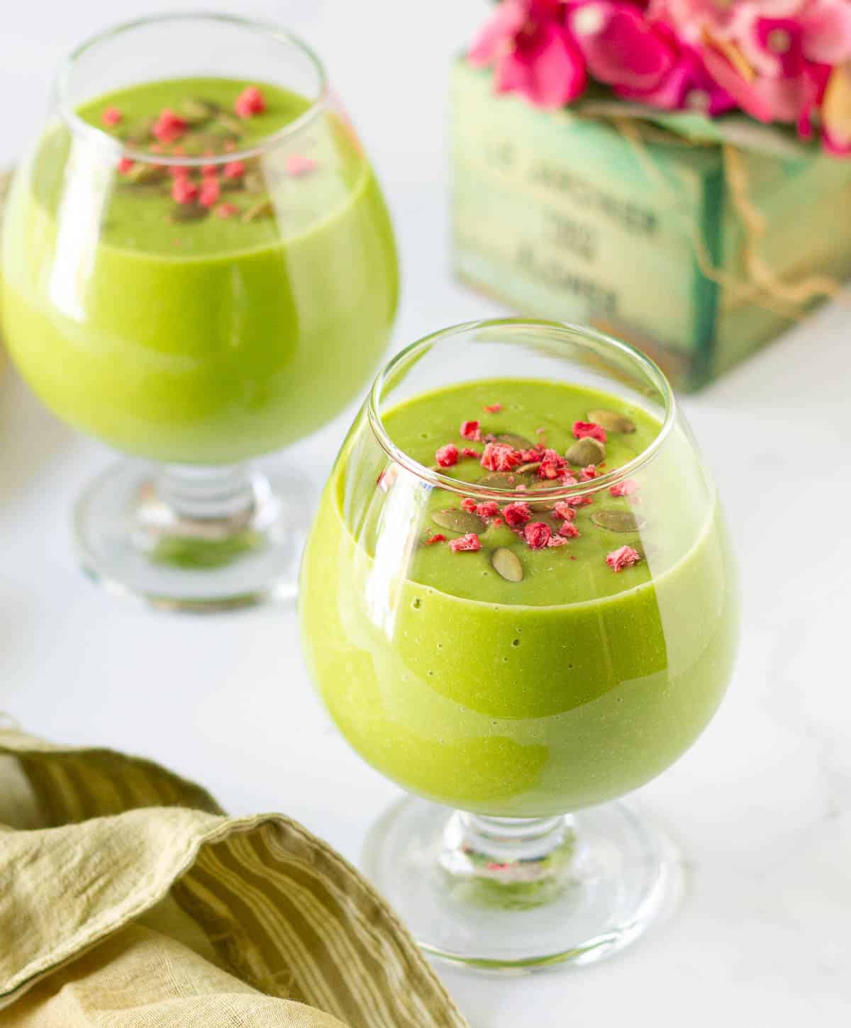 Mango smoothie with matcha in 2 glasses with a napkin and flowers.
