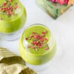mango matcha smoothie topped with dried raspberries and pumpkin seeds in 2 glasses.