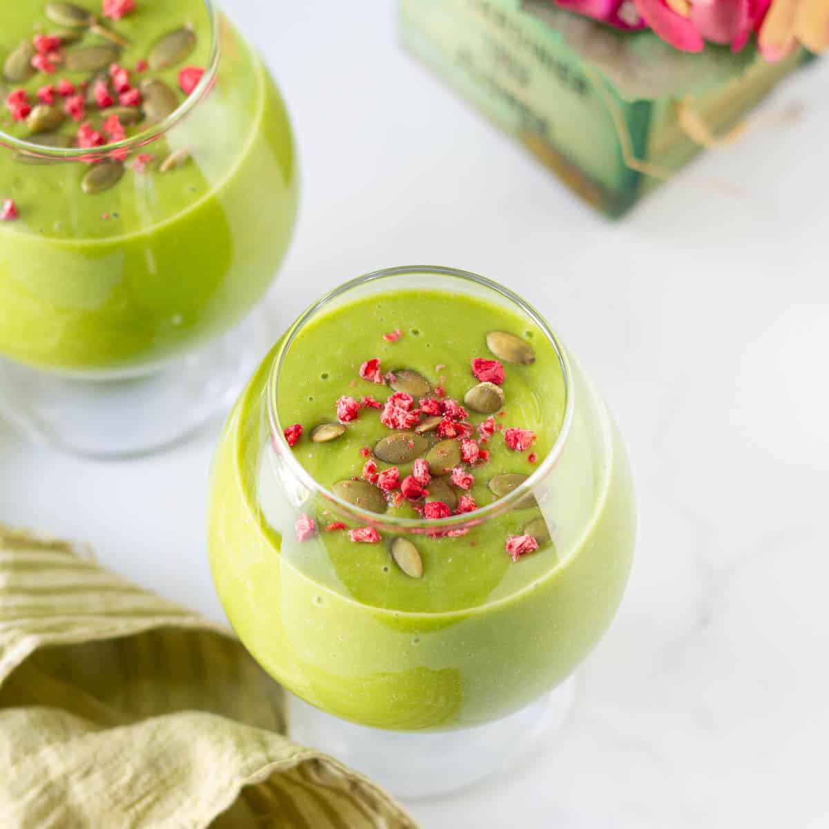 mango matcha smoothie topped with dried raspberries and pumpkin seeds in 2 glasses.