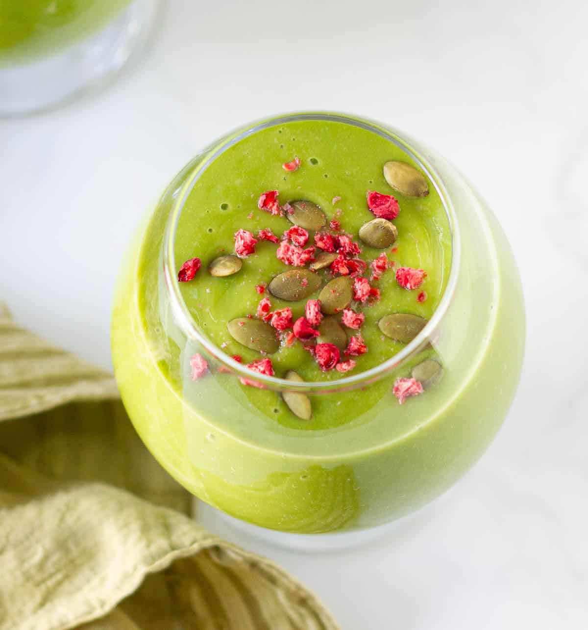 Matcha smoothie topped with dried raspberries and pumpkin seeds in a glass.