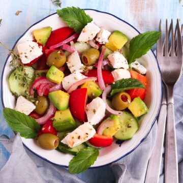 Greek salad with avocado in a bowl with 2 forks on the side.