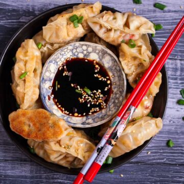 Tofu Potstickers in a bowl with dipping sauce in the center and red chopsticks.
