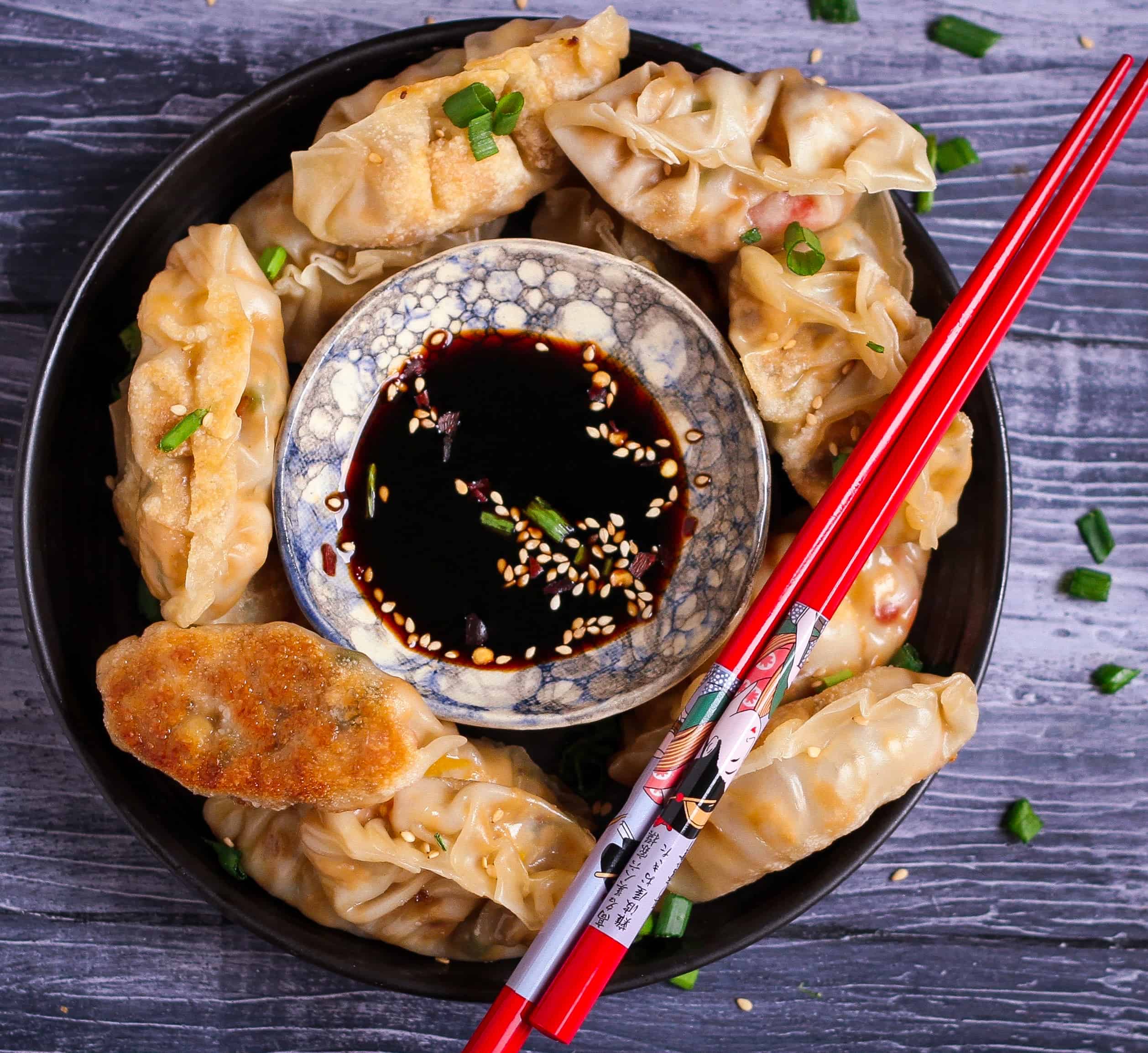 Tofu Potstickers in a bowl with dipping sauce and red chopsticks.