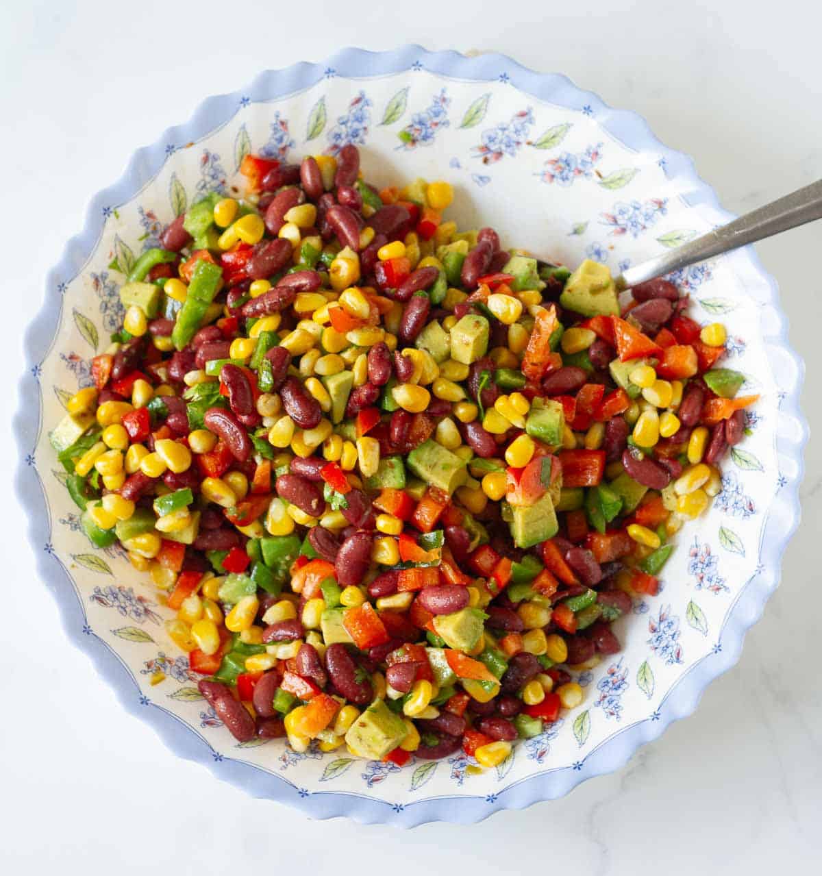 A bowl of corn bean salad with a spoon in the bowl.