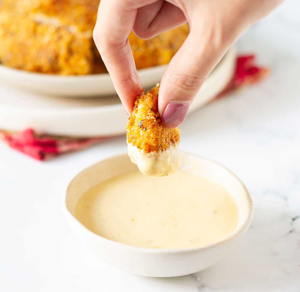 A hand holding a chicken nugget dipped in sauce.