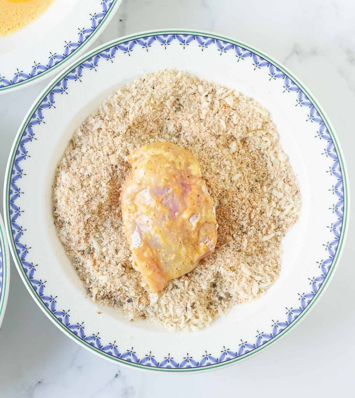 A chicken piece in a bowl of panko breadcrumbs.