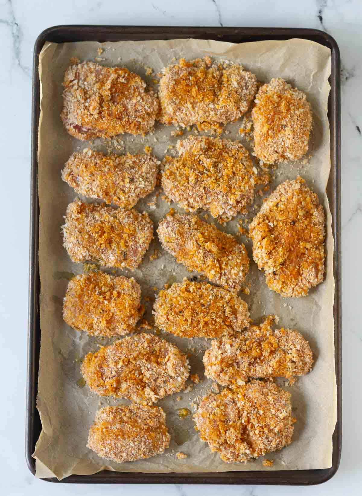 Panko breadbrumb coated chicken pieces on a parchment-lined tray.