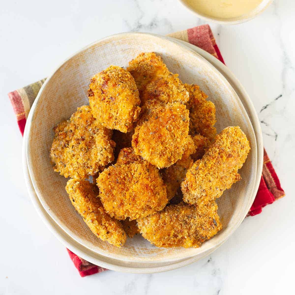 A bowl of chicken nuggets with sauce on the side.