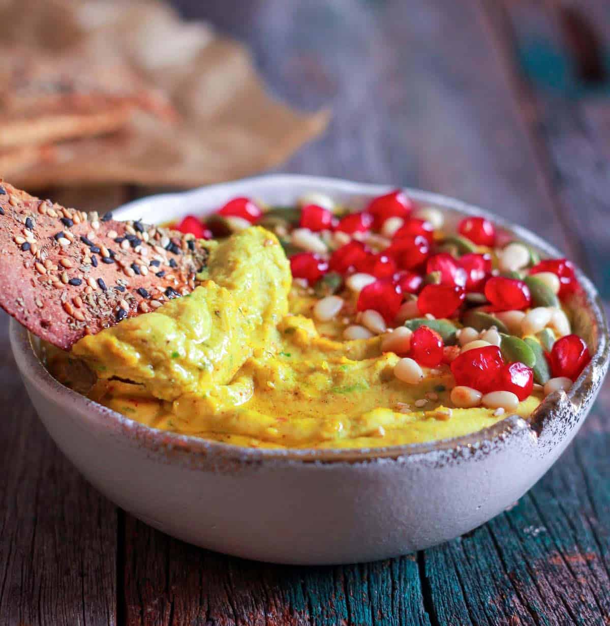 Hummus scooped on a cracker on top of a bowl of hummus.