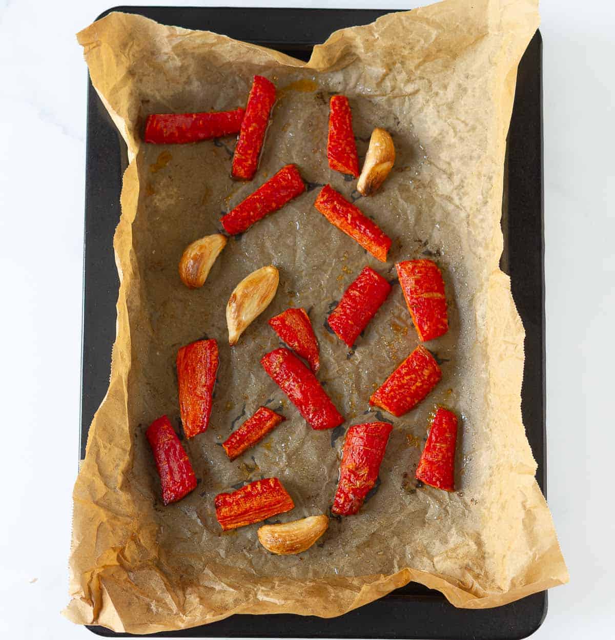 Roasted carrots and garlic on a parchment paper-lined baking tray.