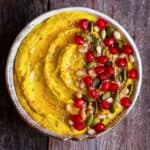 Hummus in a bowl with pomegranate arils, nuts and pumpkin seeds.