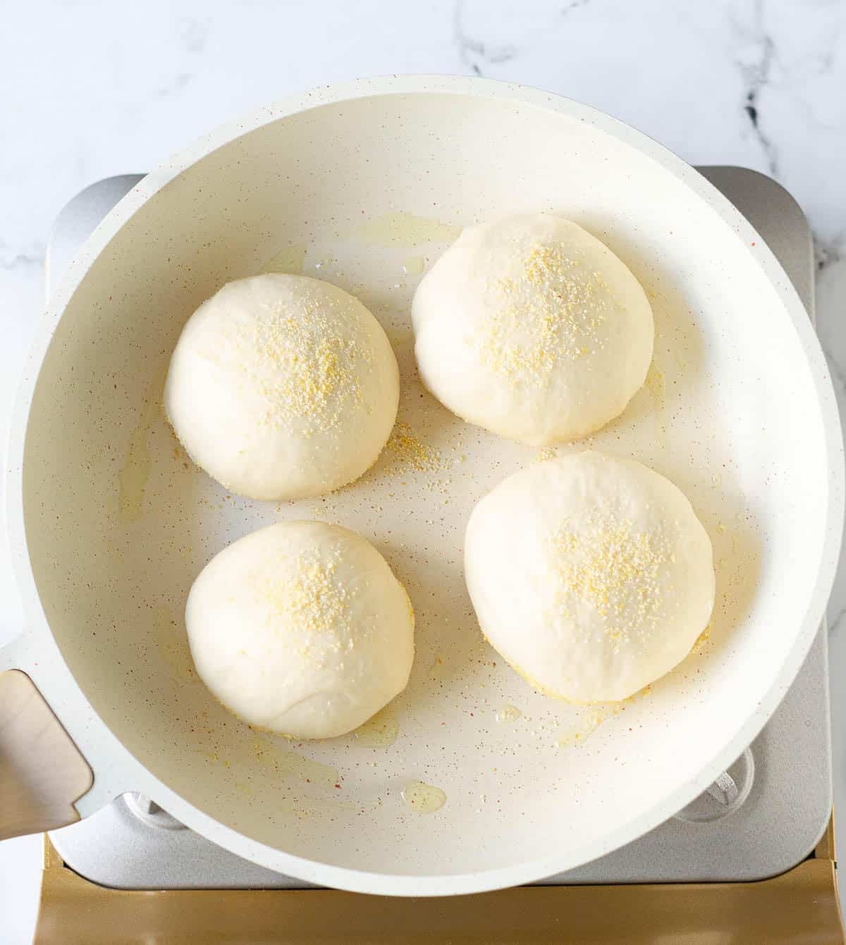 4 English muffins dough balls in a white skillet.