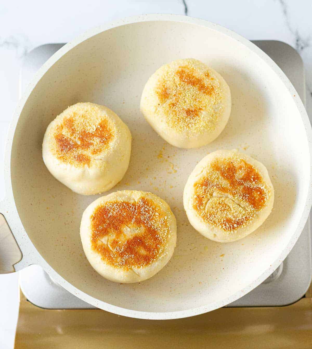 4 English muffins cooked on a white skillet.