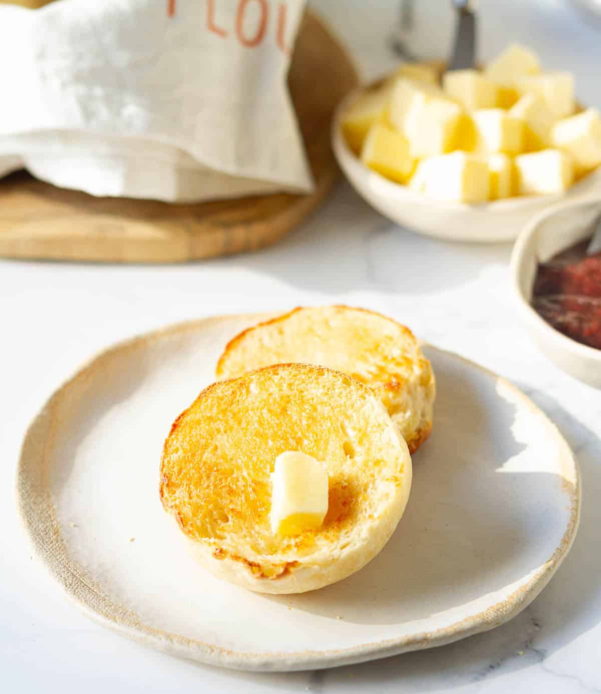 An English muffin cut in half and spread with butter on a small plate.