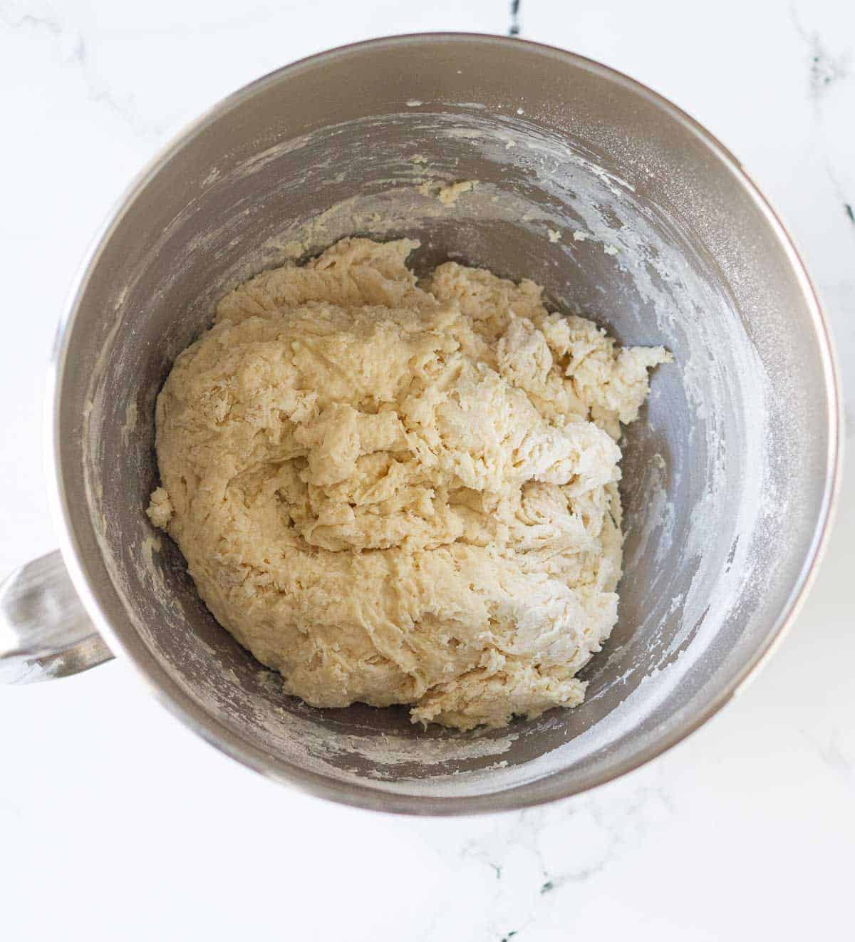 A scraggy dough for English muffins in a mixing bowl.