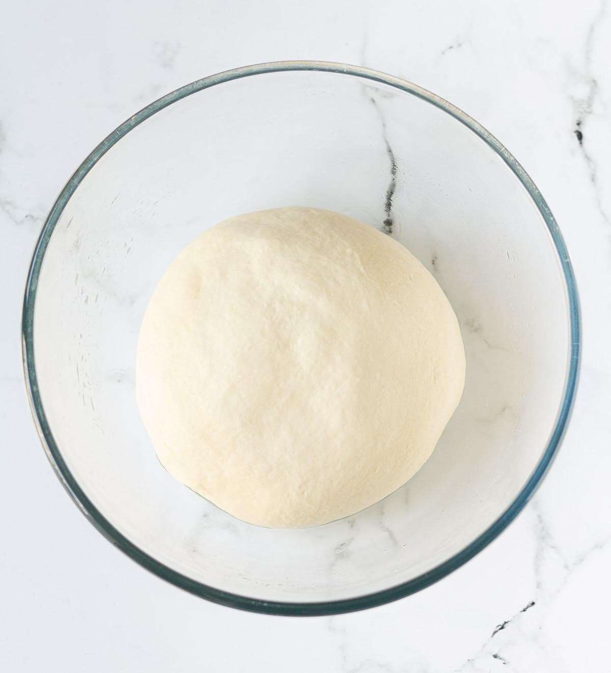 Kneaded dough for English muffins in a glass mixing bowl.
