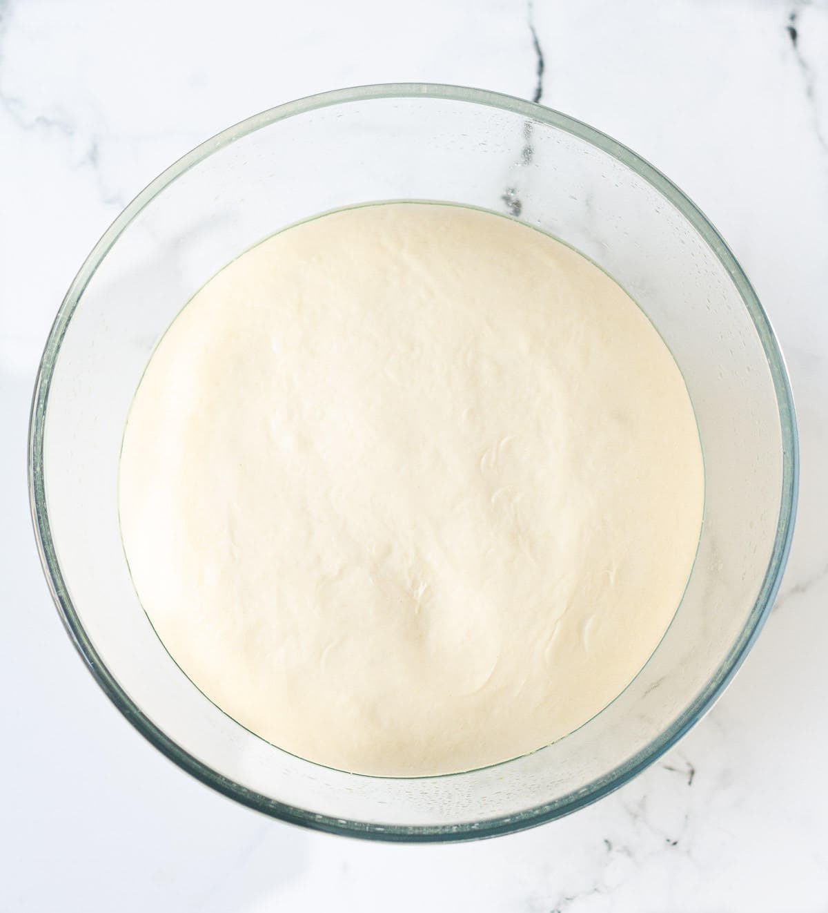 Proofed bread dough in a glass mixing bowl.