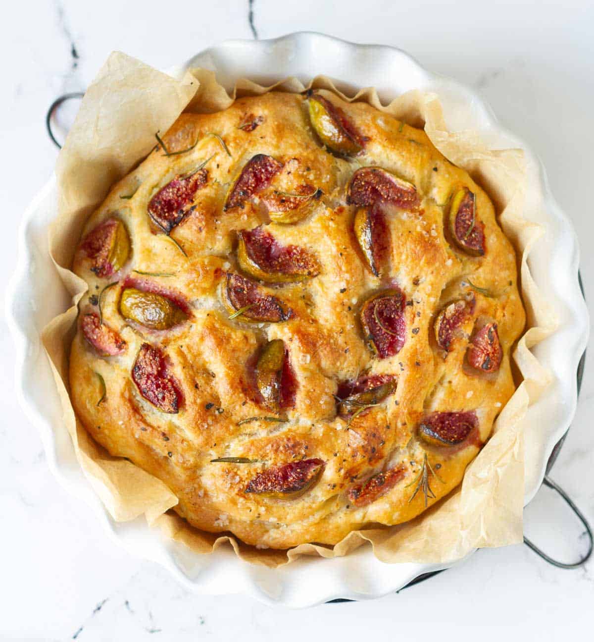 Baked focaccia with figs and rosemary in a round dish.