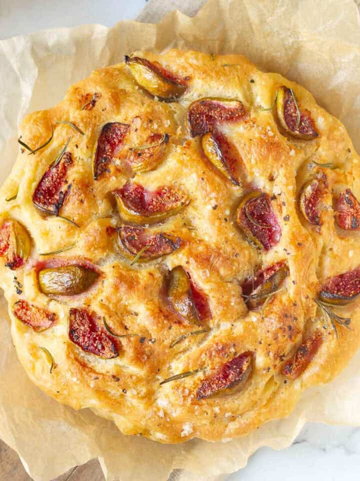 A loaf of focaccia with figs and rosemary on parchment paper.