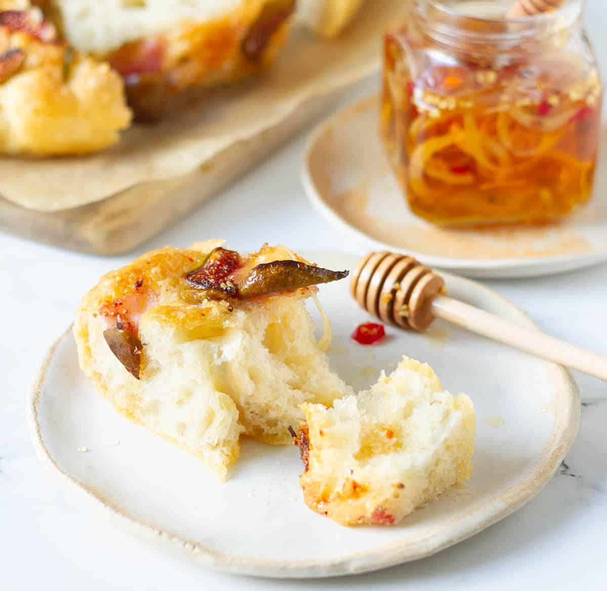 A slice of focaccia cut into 2 with a honey server on a plate.
