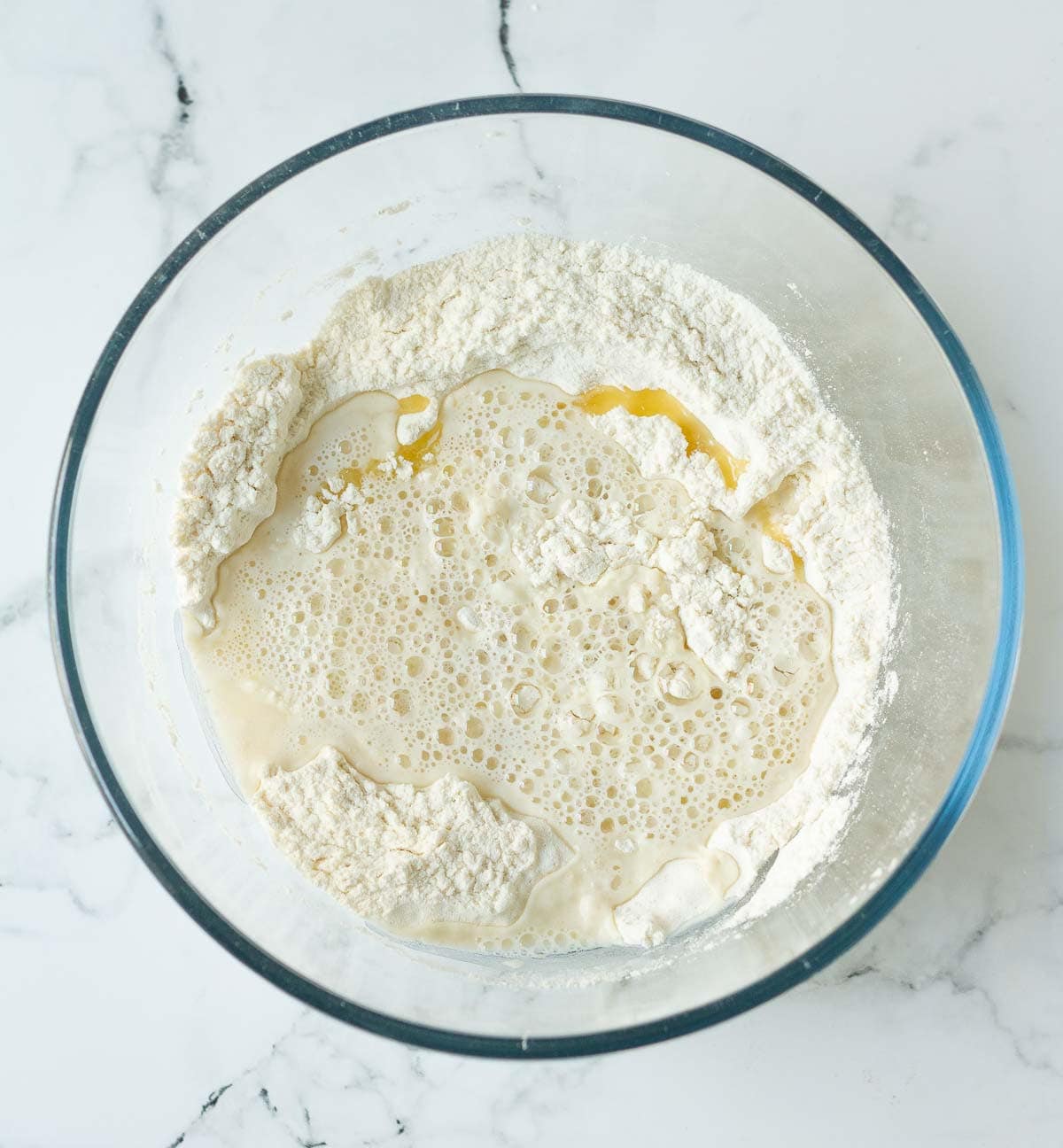 Water and olive oil on top of dry ingredients in a mixing bowl.