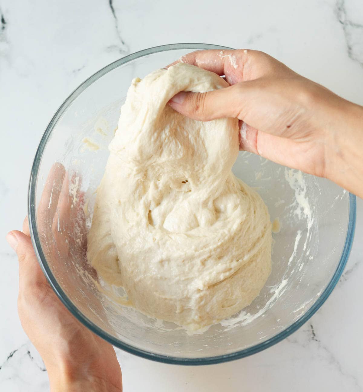 A hand stretching dough in a mixing bowl.