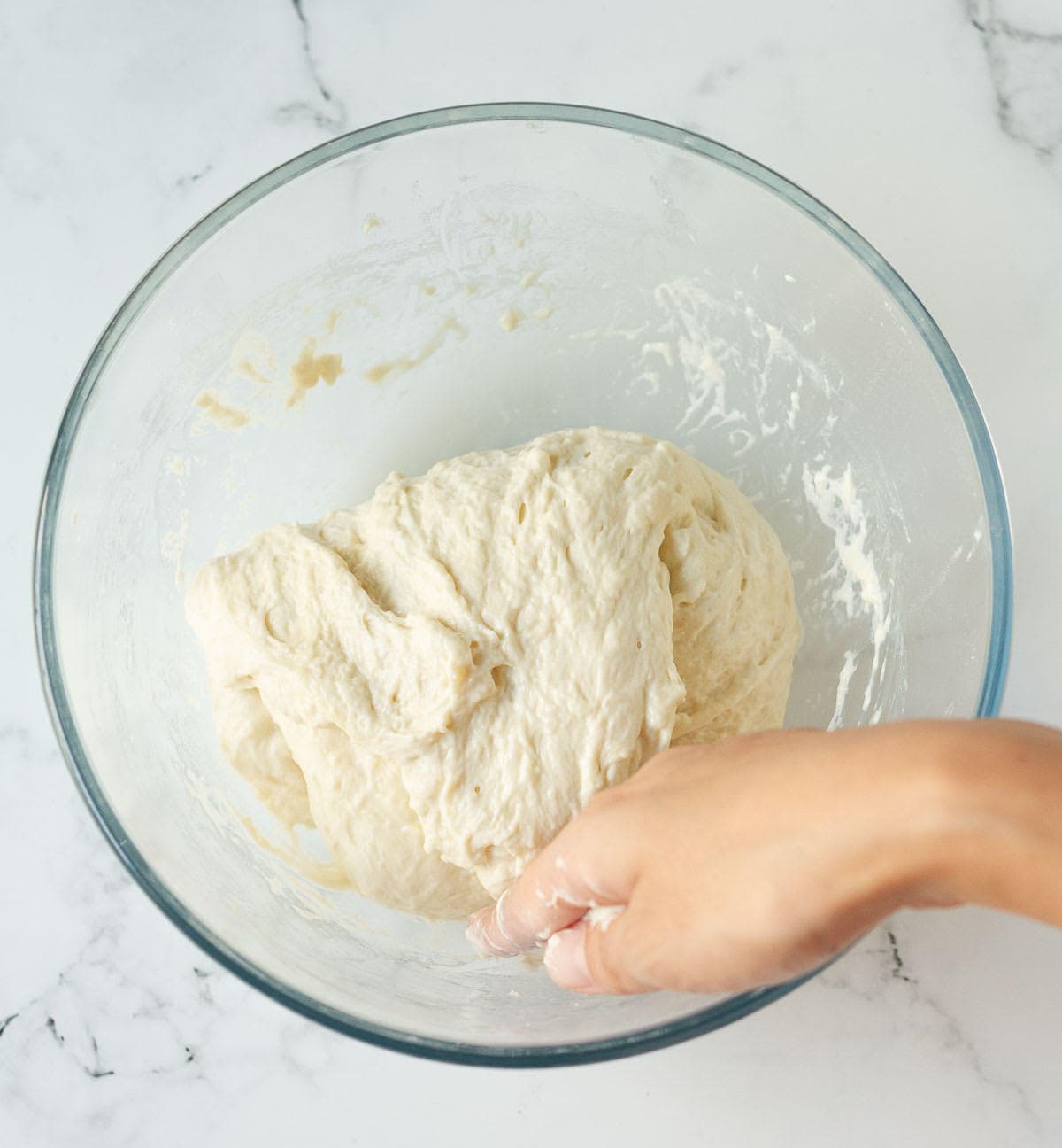 A hand folding over dough in a mixing bowl.