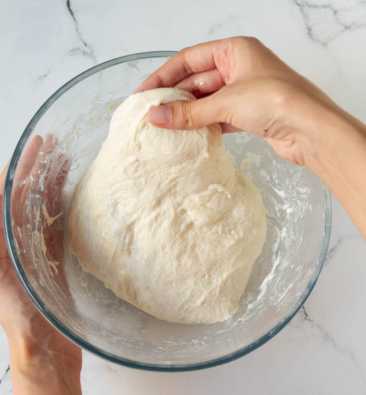 A hand pulling a piece of dough in a mixing bowl.