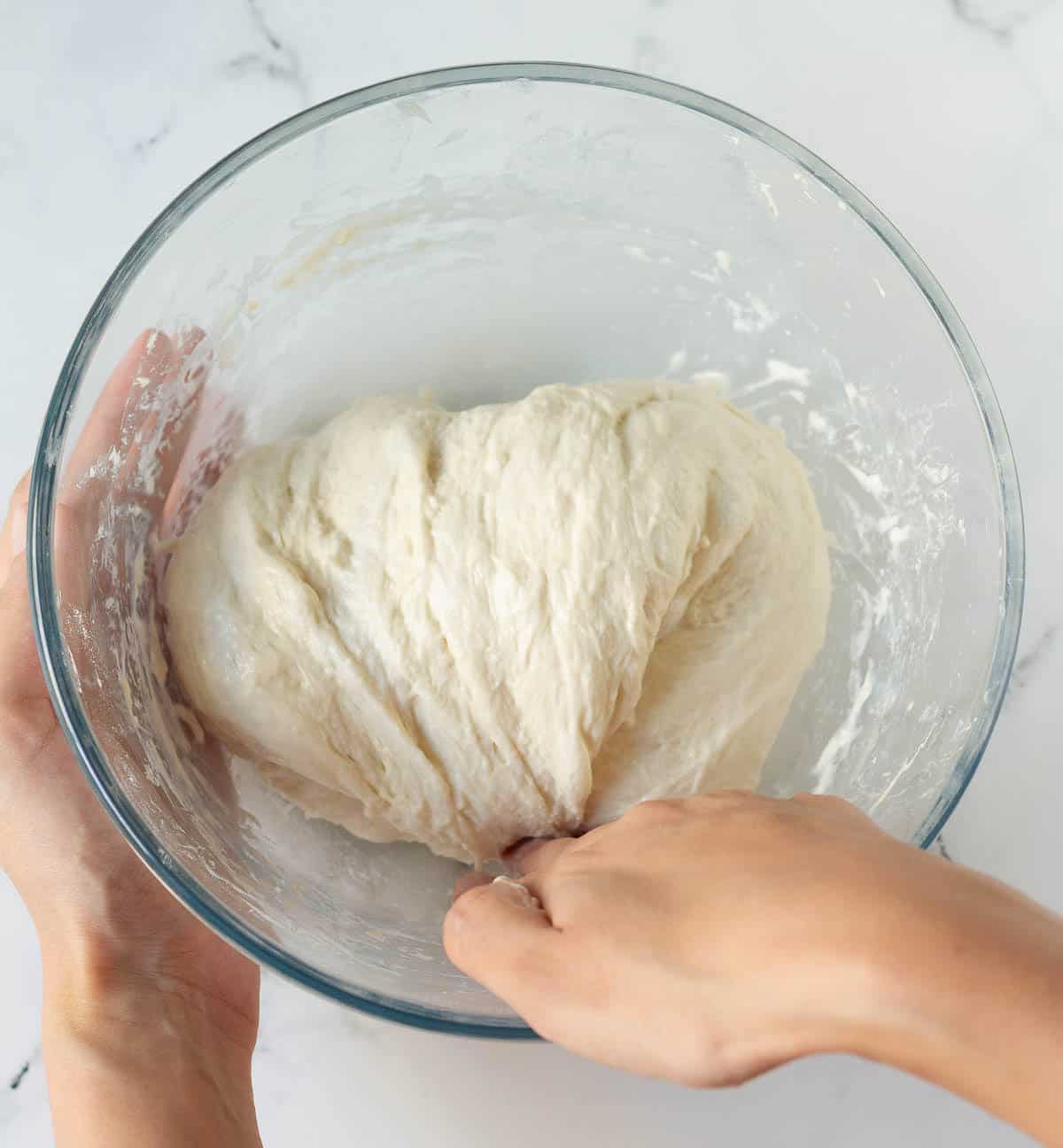 A hand folding over dough in a bowl.