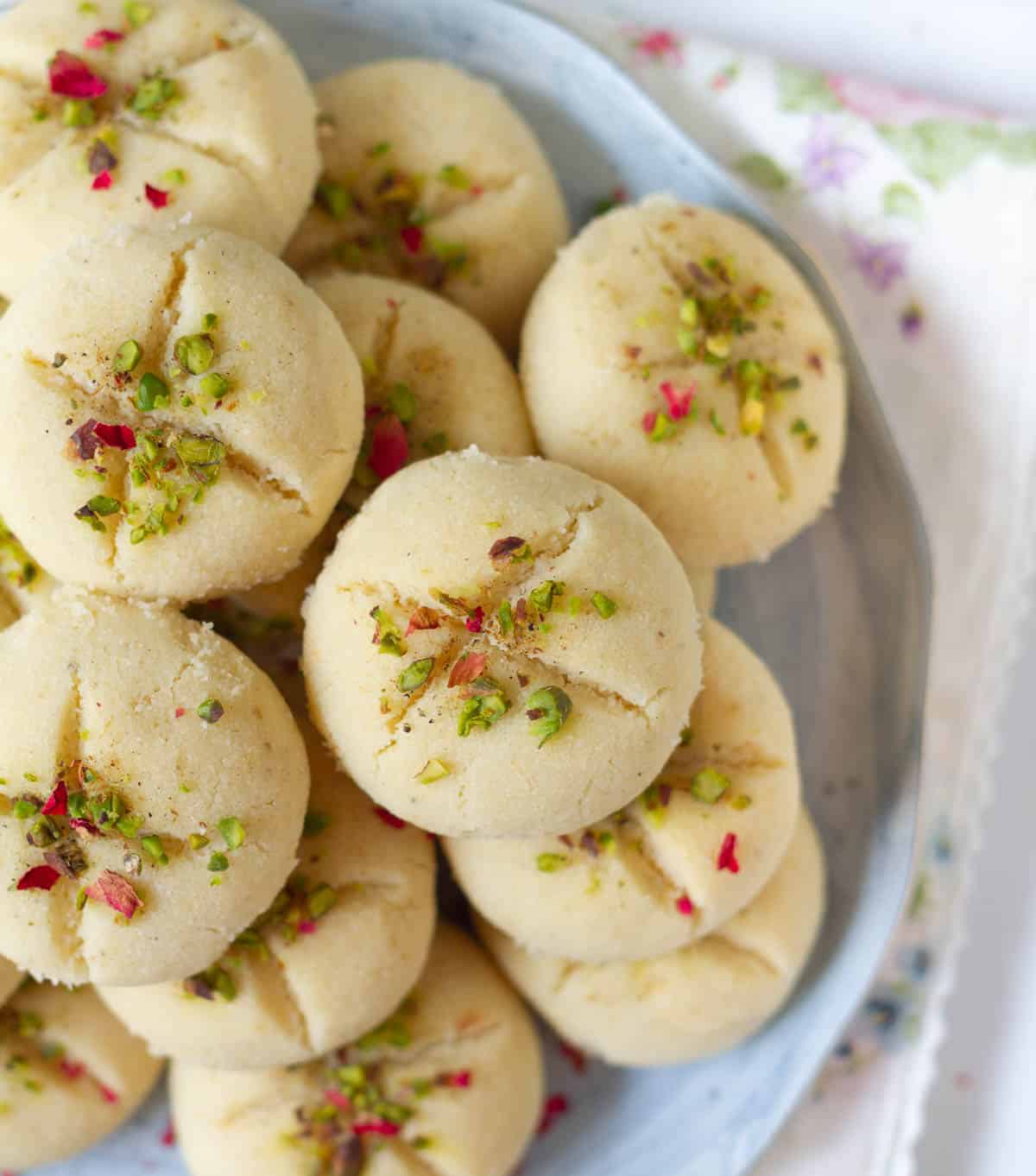 Cookies topped with dried rose petals and chopped pistachios on a plate.