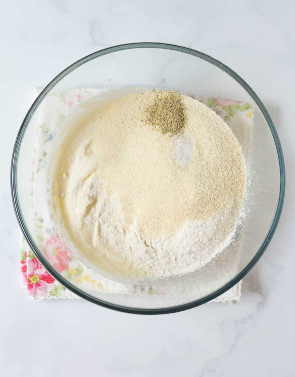 Flour, semolina, and cardamom powder on top of ghee-sugar mixture in a bowl.