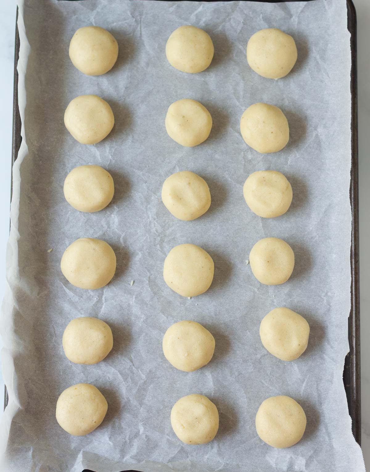 Shaped cookie dough balls on a parchment paper lined tray.