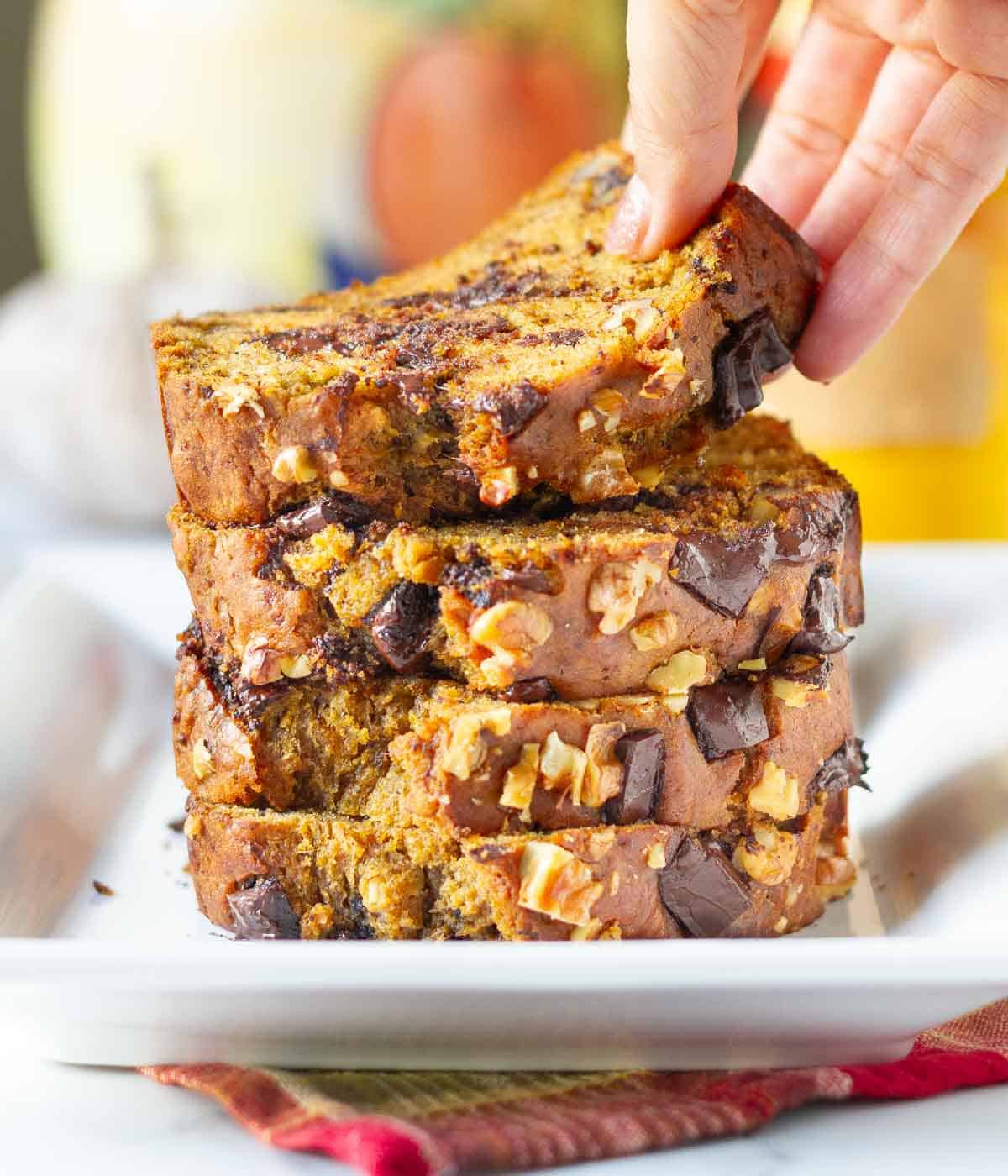 A stack of 4 pumpkin banana bread slices with a hand picking up one.