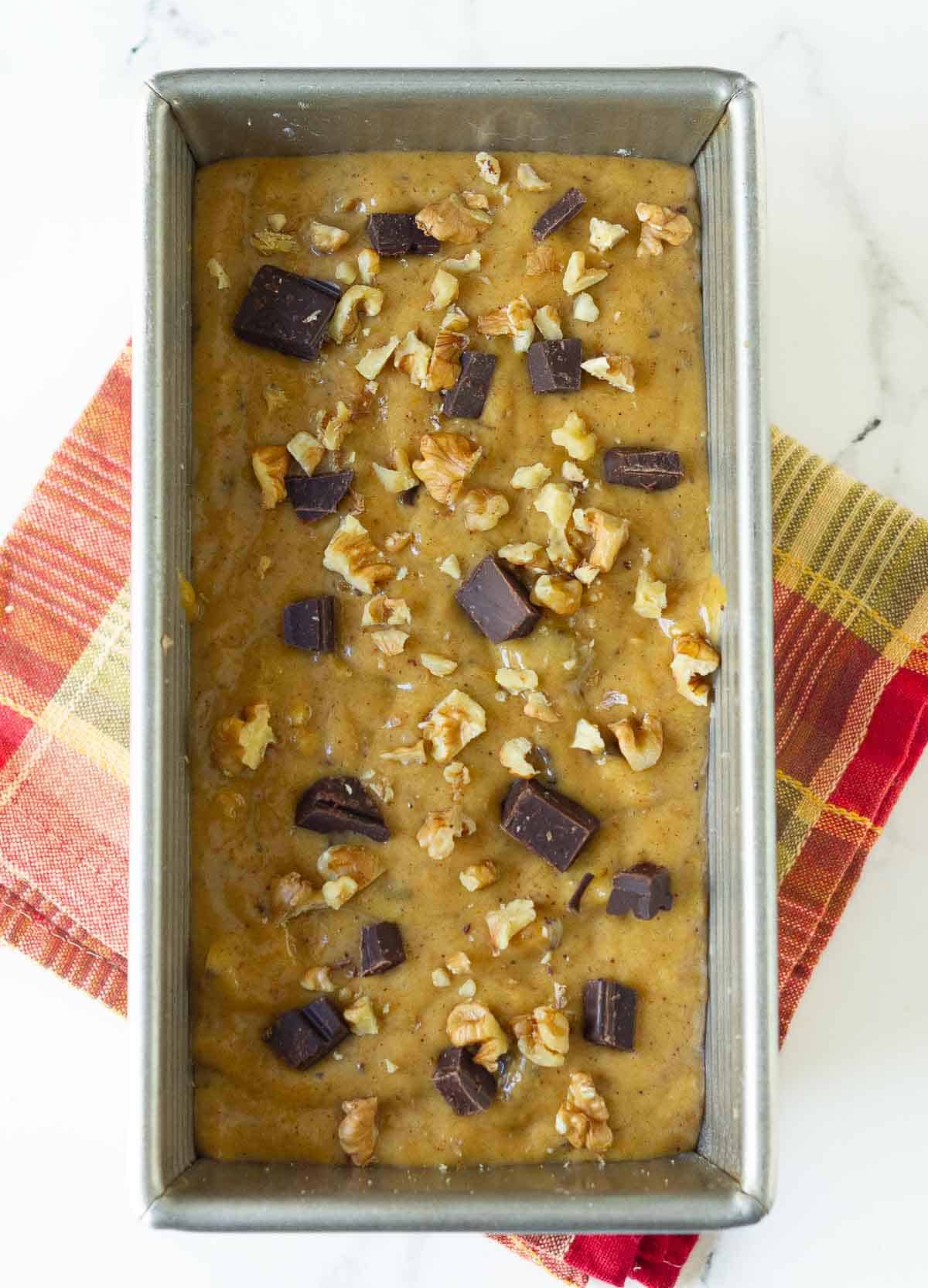 Cake batter with chocolate chips and walnuts in a cake pan.