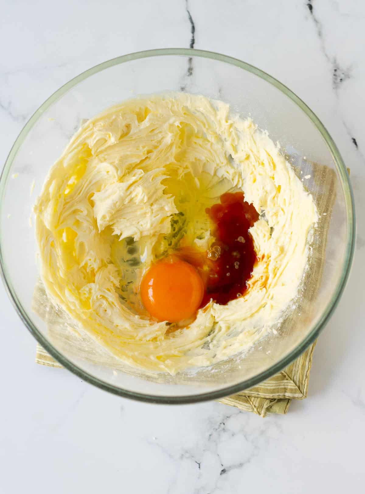 Egg and vanilla extract on whipped butter and sugar mixture in a bowl.